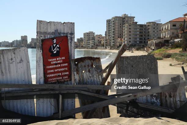 Former, decaying hotel buildings stand beyond a makeshift barrier and a Turkish military sign inside the "Forbidden Zone" of Varosha district on...