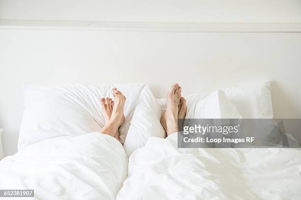 a couple lying in a bed with their feet sticking out from underneath the covers - duvet stock pictures, royalty-free photos & images