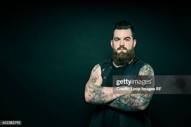 studio portrait of a bearded man with tattooed arms - motociclista fotografías e imágenes de stock