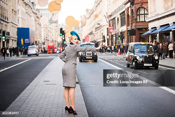 a stylish young woman dressed in 1930s style clothing hailing a taxi on regent street in london - 1930s woman stock pictures, royalty-free photos & images