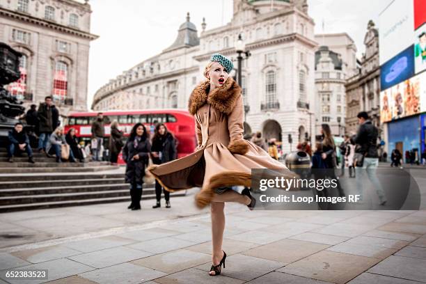 a stylish young woman dressed in 1930s style clothing twirling around by the statue of eros at piccadilly circus - women in the 1920's foto e immagini stock