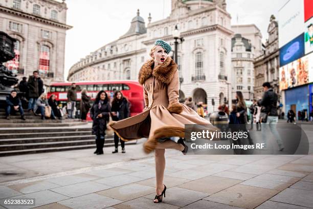 a stylish young woman dressed in 1930s style clothing twirling around by the statue of eros at piccadilly circus - picadilly circus stockfoto's en -beelden