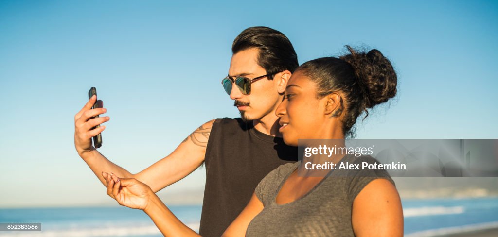 Young couple, Latino man and girl, take selfie on beach