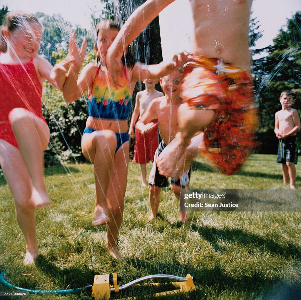 Children Jump Over Sprinkler