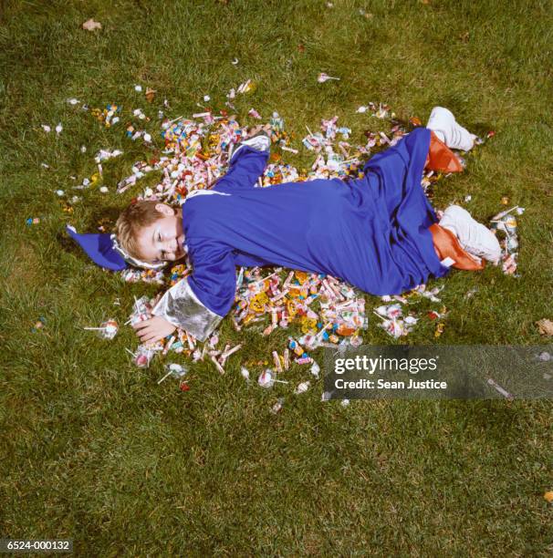 boy in costume lying on candy - halloween candy stock-fotos und bilder