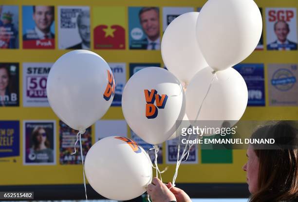 Supporter of Dutch Prime Minister and leader of the People's Party for Freedom and Democracy holds balloons in front of an electoral poster board, in...