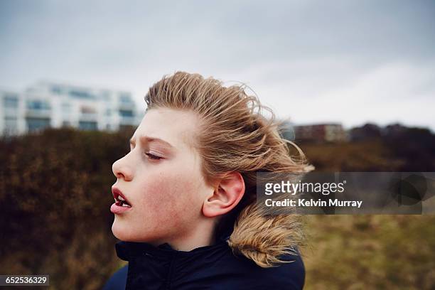 A boys hair is blown back by wind on overcast day