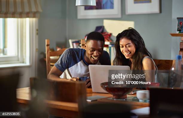 couple laughing at footage on laptop at breakfast - mixed race person stock photos et images de collection
