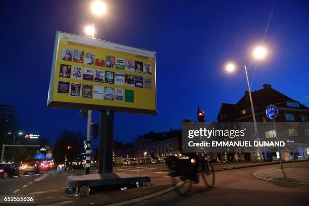 Dutch people cycles by an electoral poster board, in The Hague, on March 12, 2017. The Dutch parliamentary elections are set to take place on March...