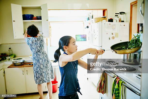 Young girl flipping green beans in pan on stove