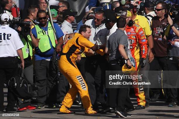 Kyle Busch, driver of the M&M's Toyota, is escorted away by a NASCAR official after an incident on pit road with Joey Logano ,, driver of the...