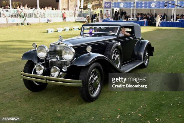 An attendee waves while driving in a 1931 Stutz DV 32 LeBaron Convertible Victoria luxury vehicle during the 2017 Amelia Island Concours d'Elegance...