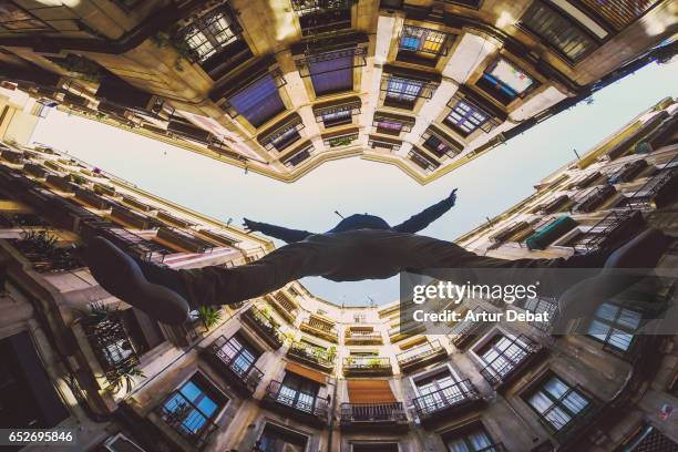 beautiful below view with wide angle lens taken from the ground and looking up of guy jumping in the beautiful streets of gothic quarter in barcelona city with narrow street and nice round square. - diminishing perspective stock-fotos und bilder