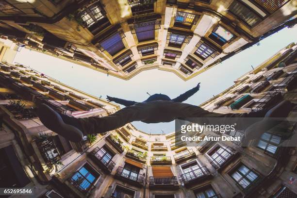 beautiful below view with wide angle lens taken from the ground and looking up of guy jumping in the beautiful streets of gothic quarter in barcelona city with narrow street and nice round square. - fish eye lens stockfoto's en -beelden