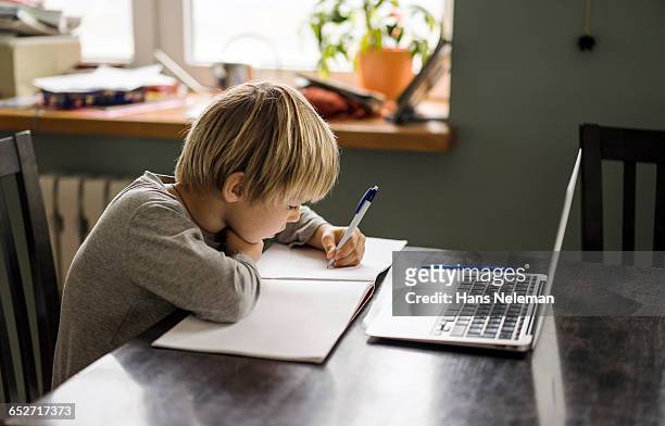 young boy making notes while using laptop - study at home foto e immagini stock