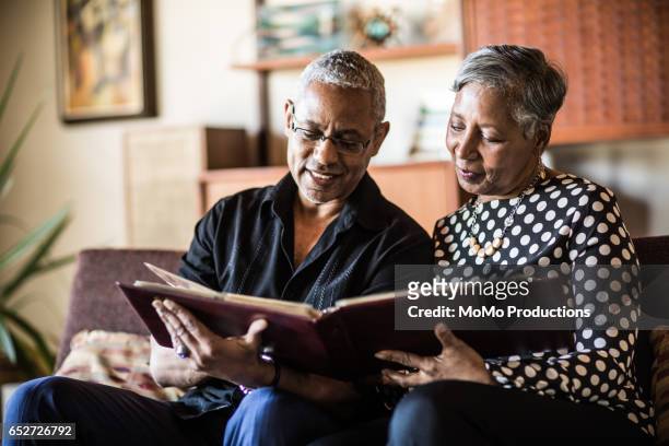 senior couple (60yrs) looking at photo album on couch at home - memories stock pictures, royalty-free photos & images