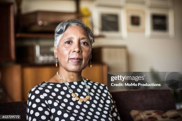 portrait of woman (60yrs) sitting on couch at home - african american woman serious stock-fotos und bilder