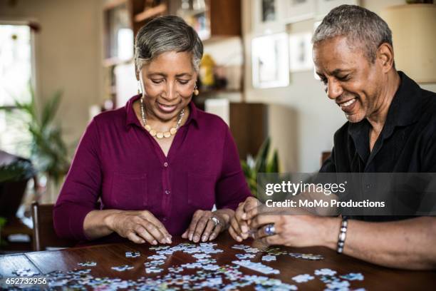 senior couple (60yrs) assembling puzzle at home - puzzel stockfoto's en -beelden