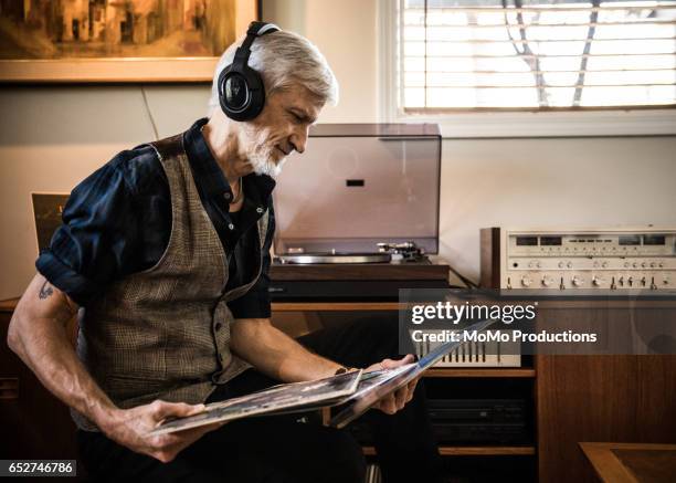 man (60yrs) playing records at home - headphones turntable stock-fotos und bilder