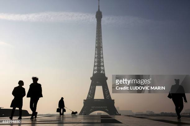 People walk on the Parvis des Droits de l'Homme square near the Eiffel tower in Paris on March 13, 2017. / AFP PHOTO / LUDOVIC MARIN