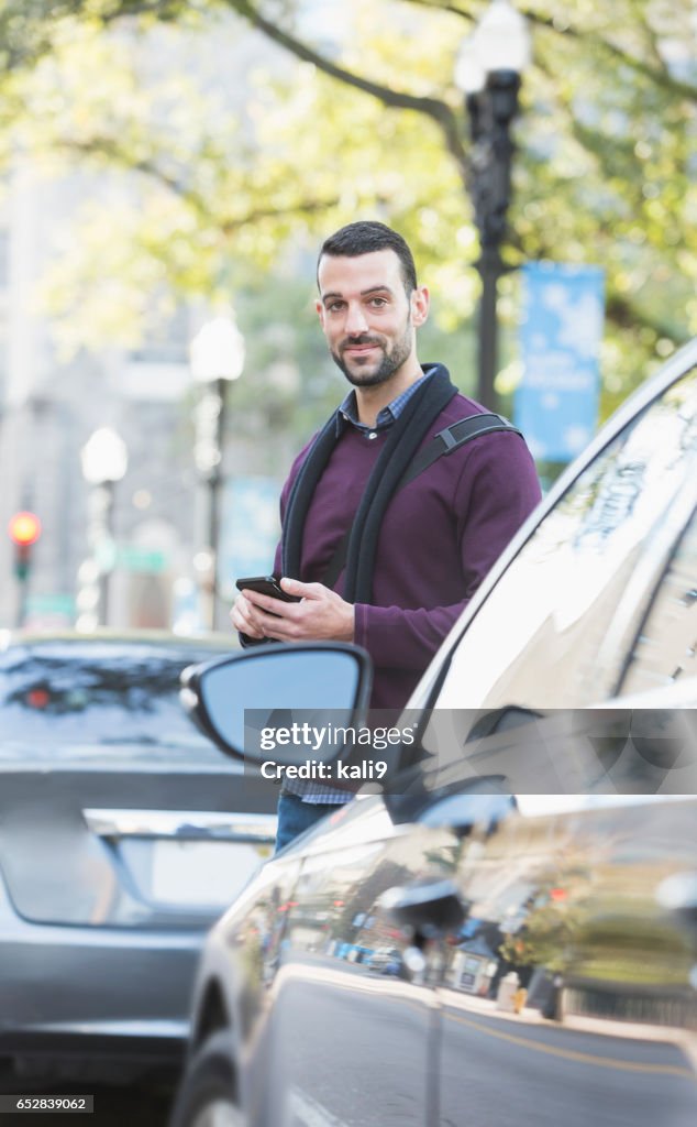 Man with mobile phone on city street, waiting for car