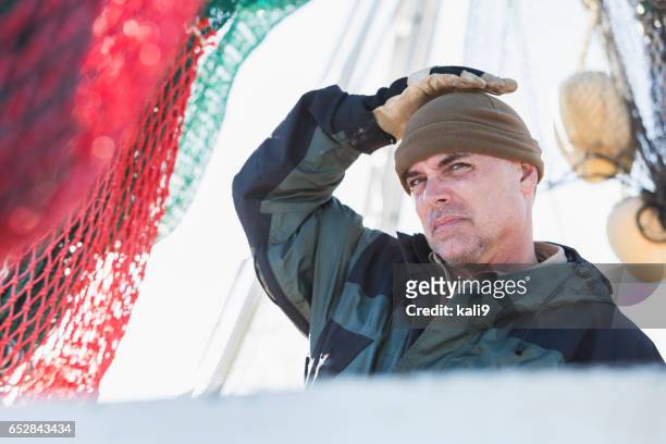 man working on commercial fishing boat putting on hat - shrimp boat stock pictures, royalty-free photos & images