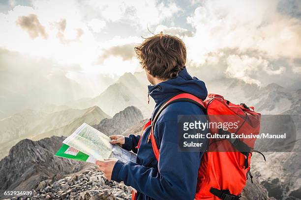 young man at summit of mountain, looking at map, mount hochwanner, wetterstein mountains, bavaria - bergsteiger mit karte und rucksack stock-fotos und bilder