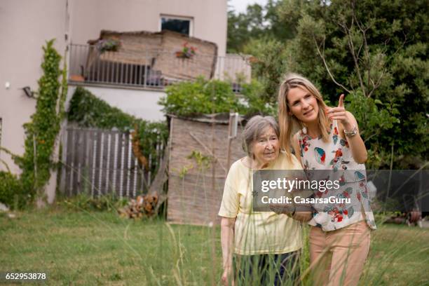 assistent in de kwekerij hebben een wandeling met senior vrouw in de tuin - woonzorg stockfoto's en -beelden