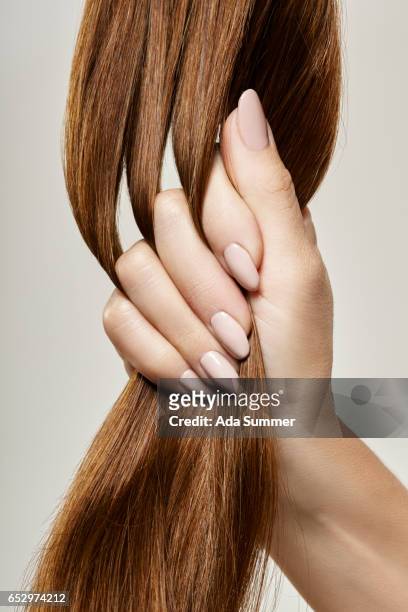 human female hand holding brown hair against gray background, close up - healthy hair stock pictures, royalty-free photos & images