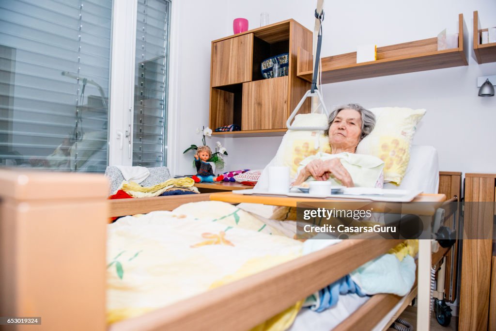 Disabilita la donna anziana che sta facendo colazione nel suo letto nella casa di riposo