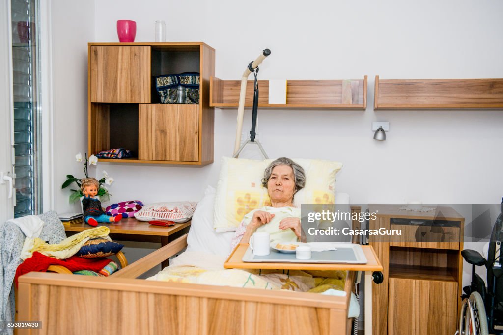 Disable Senior Woman Having Breakfast In Her Bed At The Retirement Home