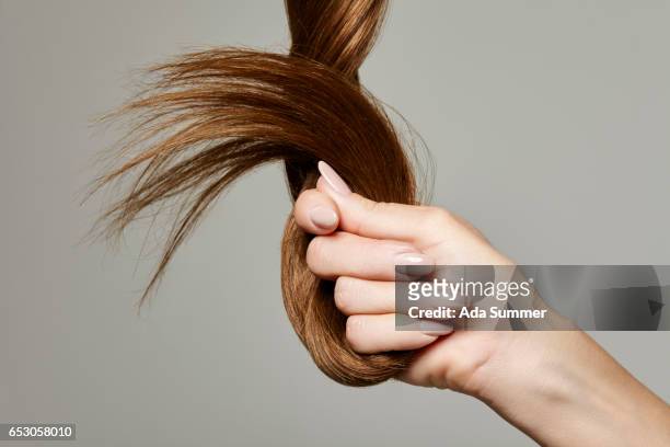human hand holding brown hair against gray background, close up - human hair stockfoto's en -beelden