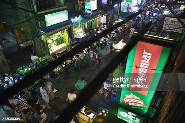 An illuminated sign for Myanmar Beer, manufactured by Myanmar Brewery Ltd., hangs above restaurants and street food stalls in the Chinatown area of...