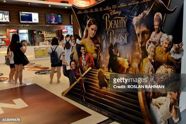 People stand near a promotional display for the film "Beauty and the Beast" at a cinema in Singapore on March 14, 2017. The film has come under fire...