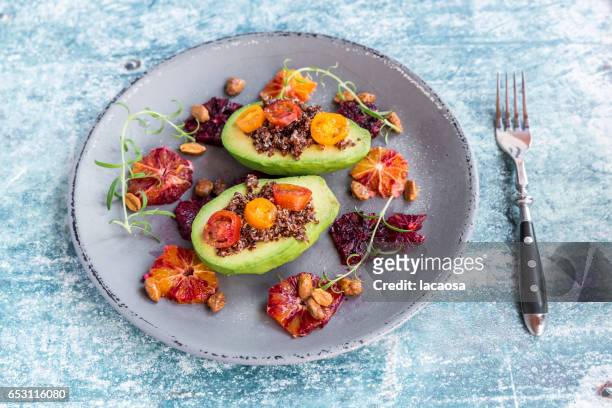 sliced avocado filled with red quinoa and tomatoes - lacaosa stock-fotos und bilder