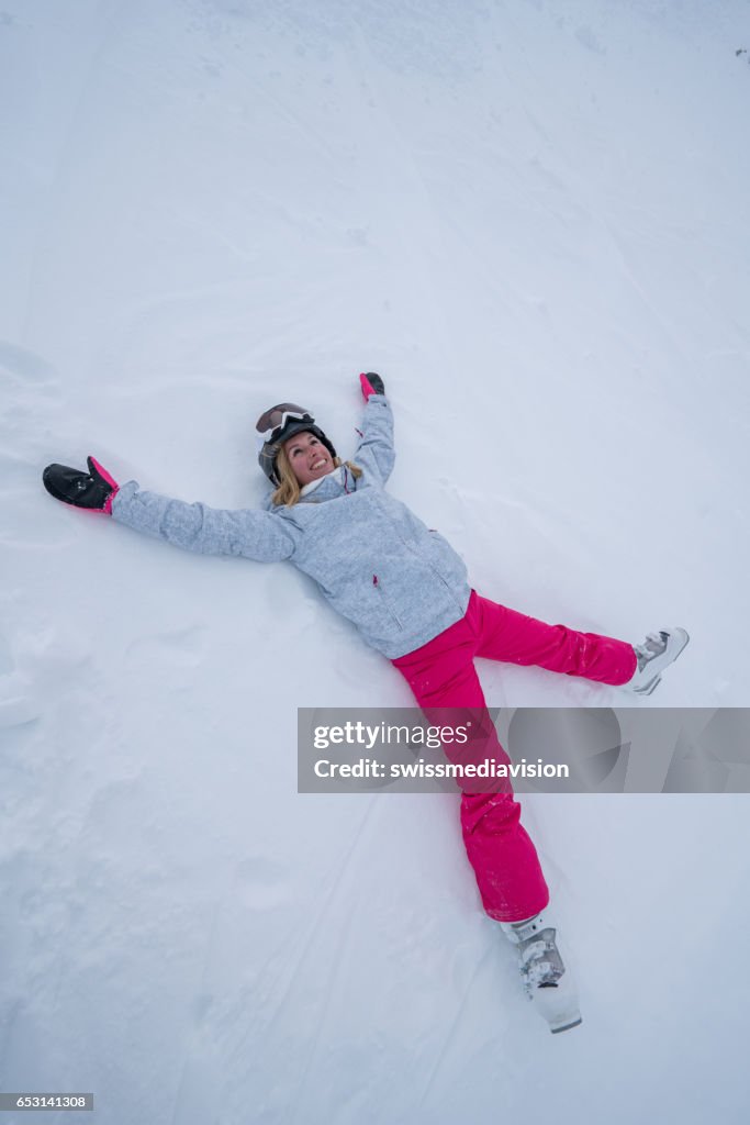 Young woman lying on snow playing snow angel