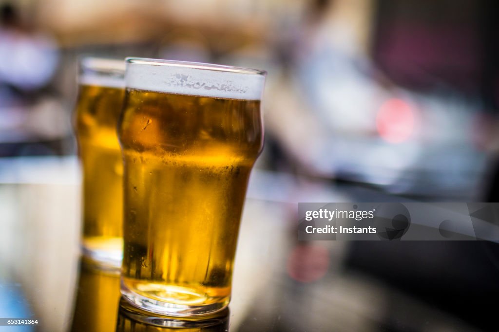 Dos vasos de cerveza rubia en una mesa, tirado en una banqueta de bar café parisino.