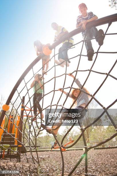 multi-ethnic elementary school children playing on playground at park. - climbing frame stock pictures, royalty-free photos & images