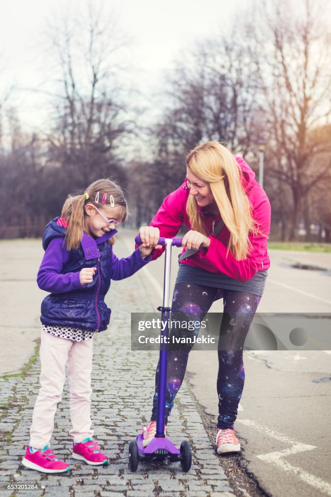 Mother showing her daughter how to ride on a push scooter