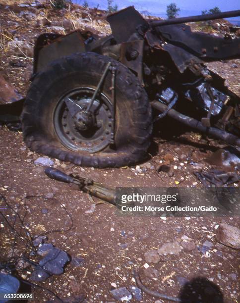 Close up view of used military weapons and a destroyed vehicle with a large deflated tire, on rocky ground in the Golan Heights, Israel, November,...