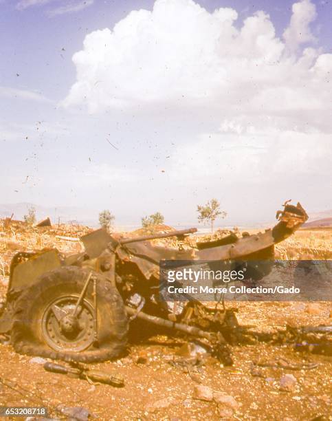 View of a burned and crushed military vehicle, with destroyed military ordnance laying nearby on rocky ground below a blue sky in the Golan Heights,...
