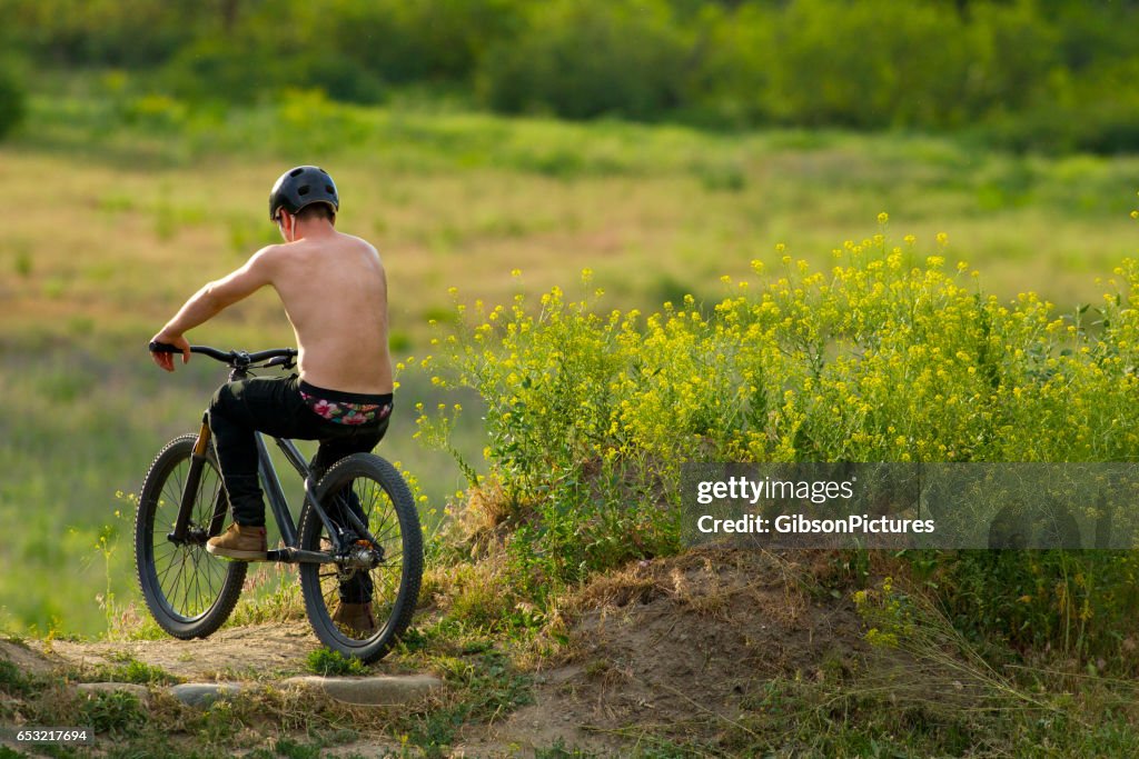 Ein Junge männliche Mountain-Bike-Fahrer liegt an der Spitze des Hügels bevor man einen großen Sprung in den Sommer.