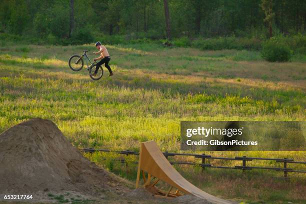 a young male mountain bike rider does a one-handed cannonball trick while riding a wooden ramp jump on a sunny day.. - hands free cycling stock pictures, royalty-free photos & images