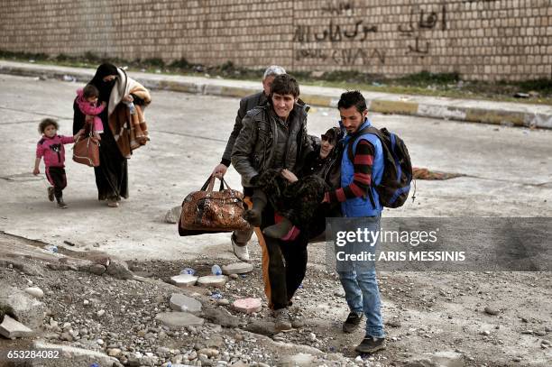 Displaced residents of western Mosul carry an elderly woman as they evacuate the area on March 14, 2017 while Iraqi government forces continue to...