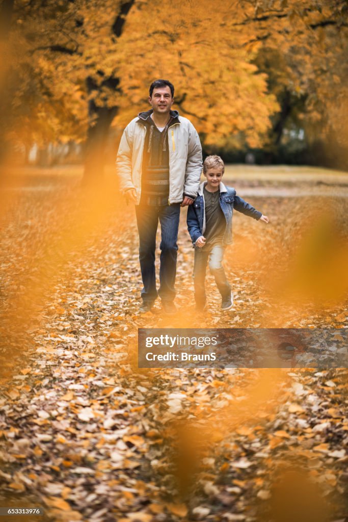 Father and son through autumn leaves in the park.