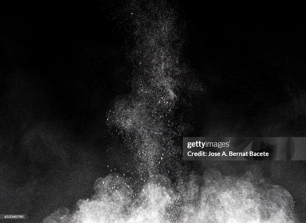 Blackground of particles of white powder in ascending movement floating in the air produced by an impact