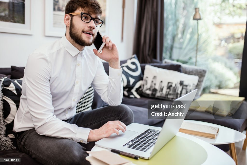 Young successful businessman talking on smartphone while getting information from laptop.