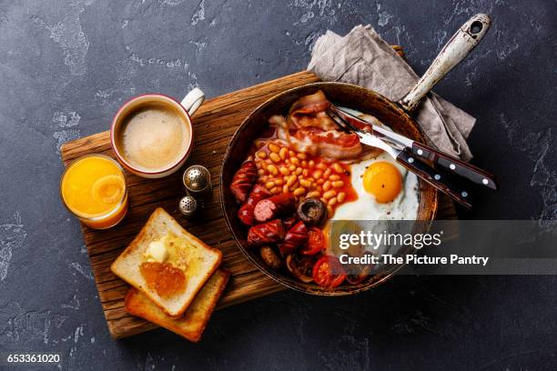 english breakfast in cooking pan with fried eggs, sausages, bacon, beans, toasts and coffee on dark stone background - full english breakfast stock pictures, royalty-free photos & images
