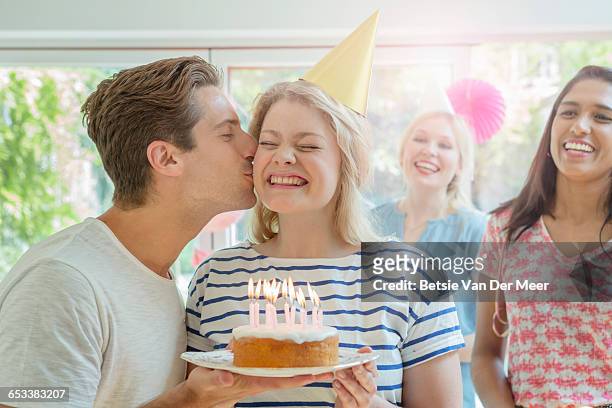 man kissing woman  holding birthday cake. - surprise birthday party stock-fotos und bilder