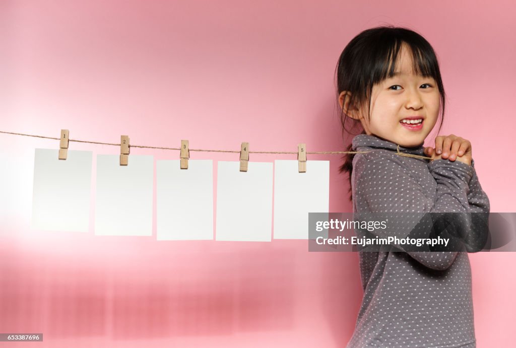 Cute girl pulling a clothesline with five sheets of white paper
